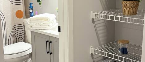 A bathroom with a toilet, a sink, a towel rack, a potted plant, and a laundry basket.