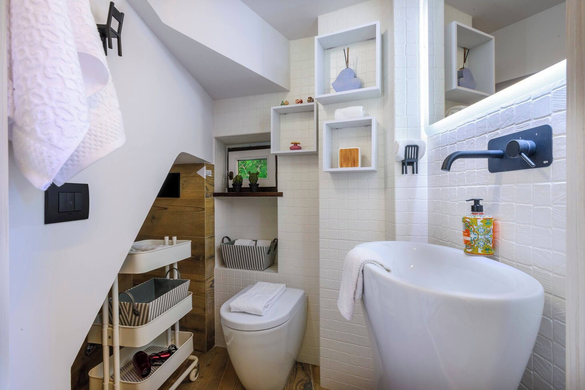 A compact bathroom with a white sink, toilet, and shelves with toiletries.