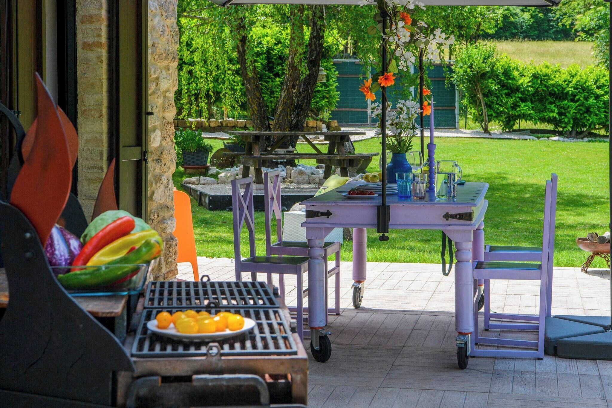 An outdoor patio with a grill, a table with a vase of flowers, and a view of a green garden.