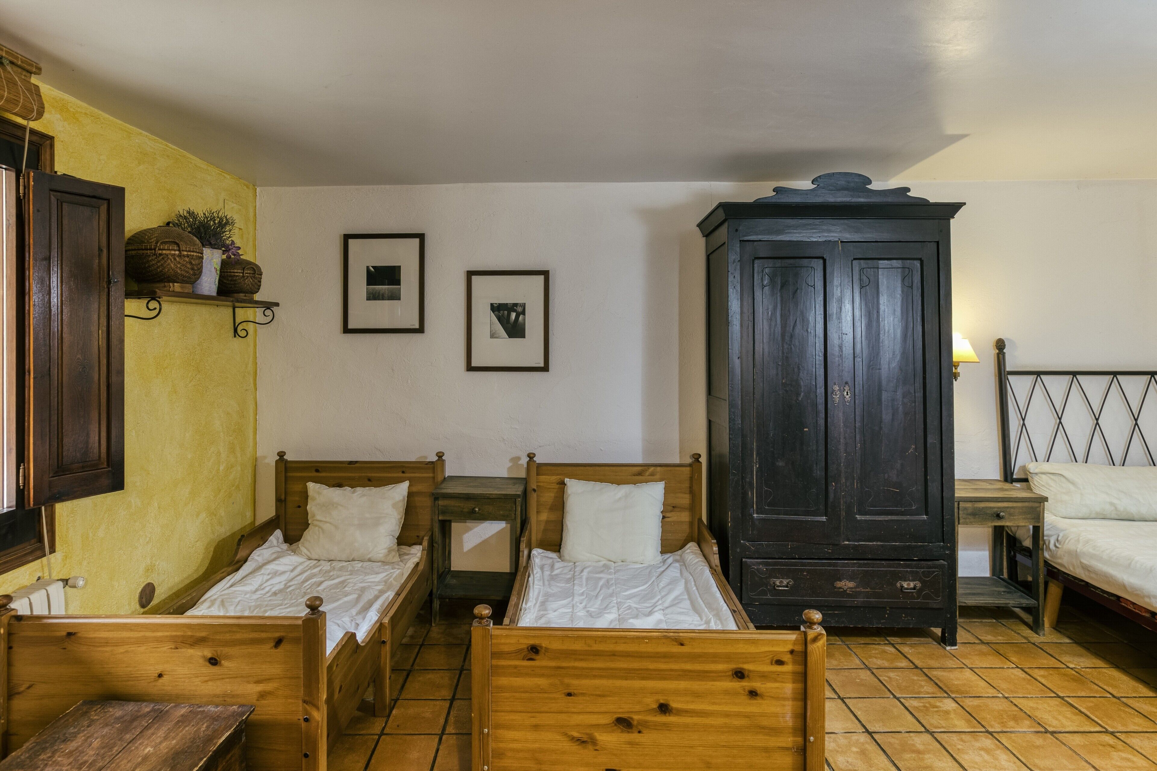 Una habitación con dos camas de madera, un armario de madera oscura, una mesita pequeña y una estantería con objetos decorativos.