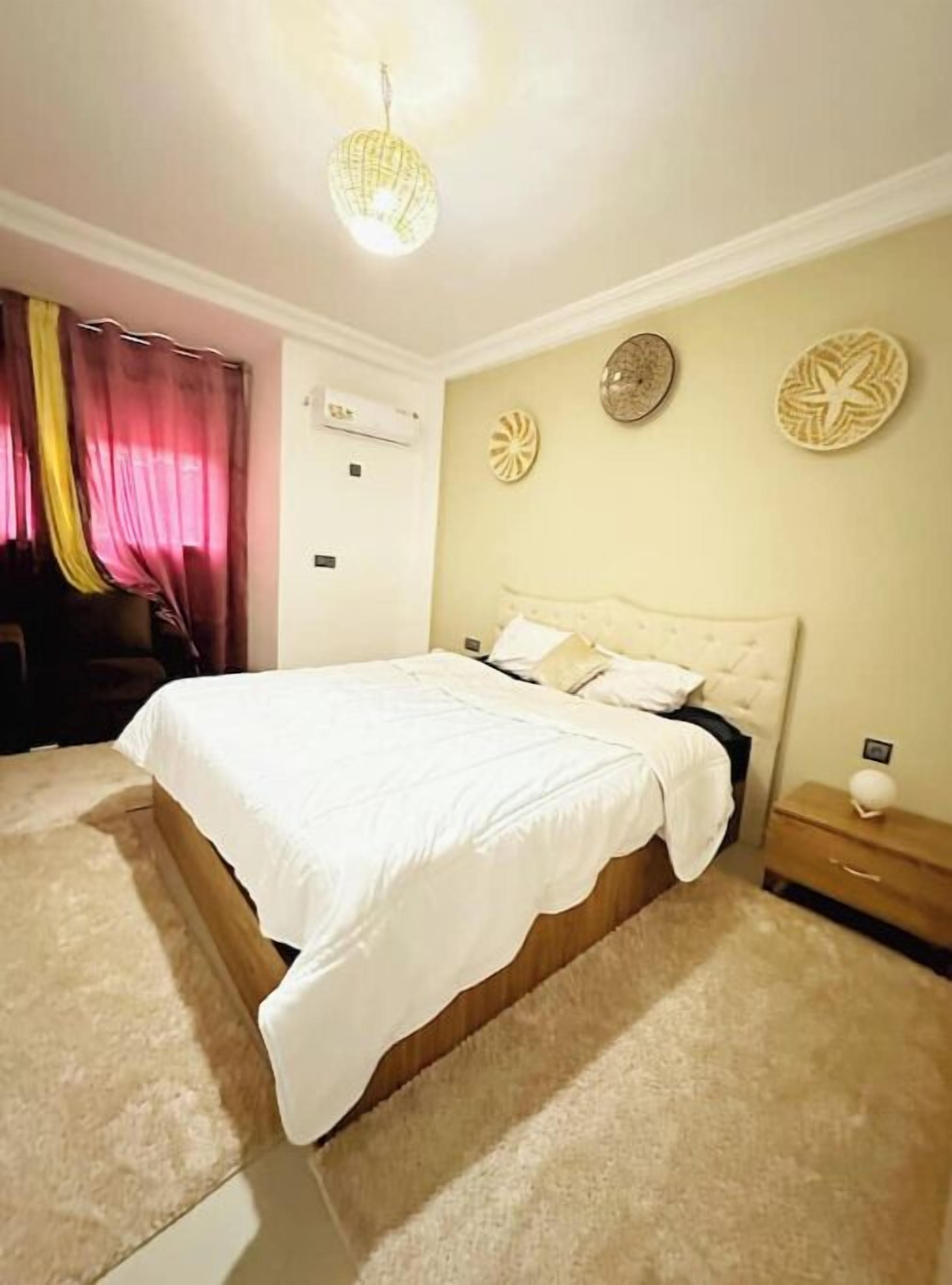 Un dormitorio con una cama grande, una mesita de noche, aire acondicionado de pared y decoración artística en la pared.