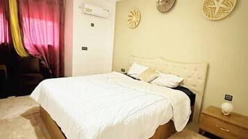 Un dormitorio con una cama grande, una mesita de noche, aire acondicionado de pared y decoración artística en la pared.