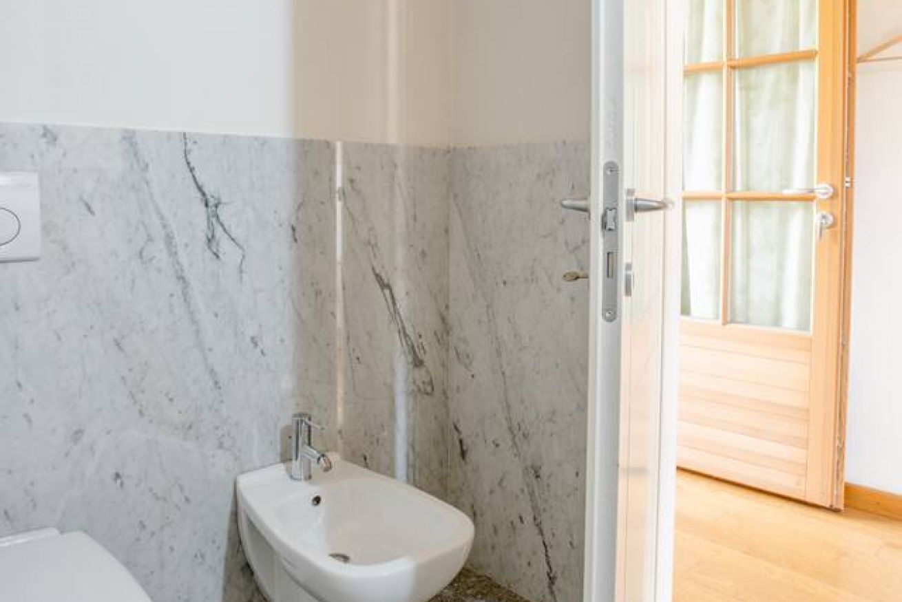 A bathroom with a bidet, marble walls, and a wooden door.