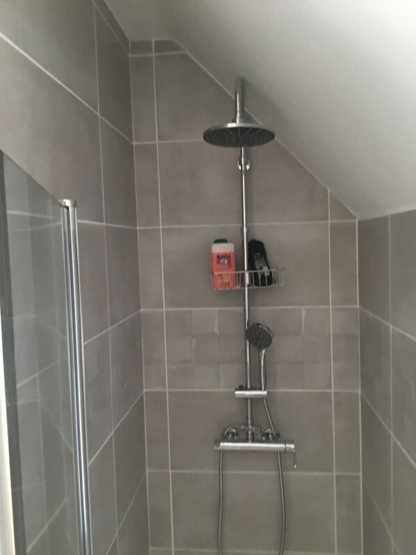 Un espacio de ducha con mampara de vidrio, cabezal de ducha de mano y panel de control en la pared.