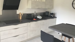 Una cocina moderna con estufa negra, lavamanos y cafetera. Hay armarios sobre el lavamanos y un reloj en la pared.