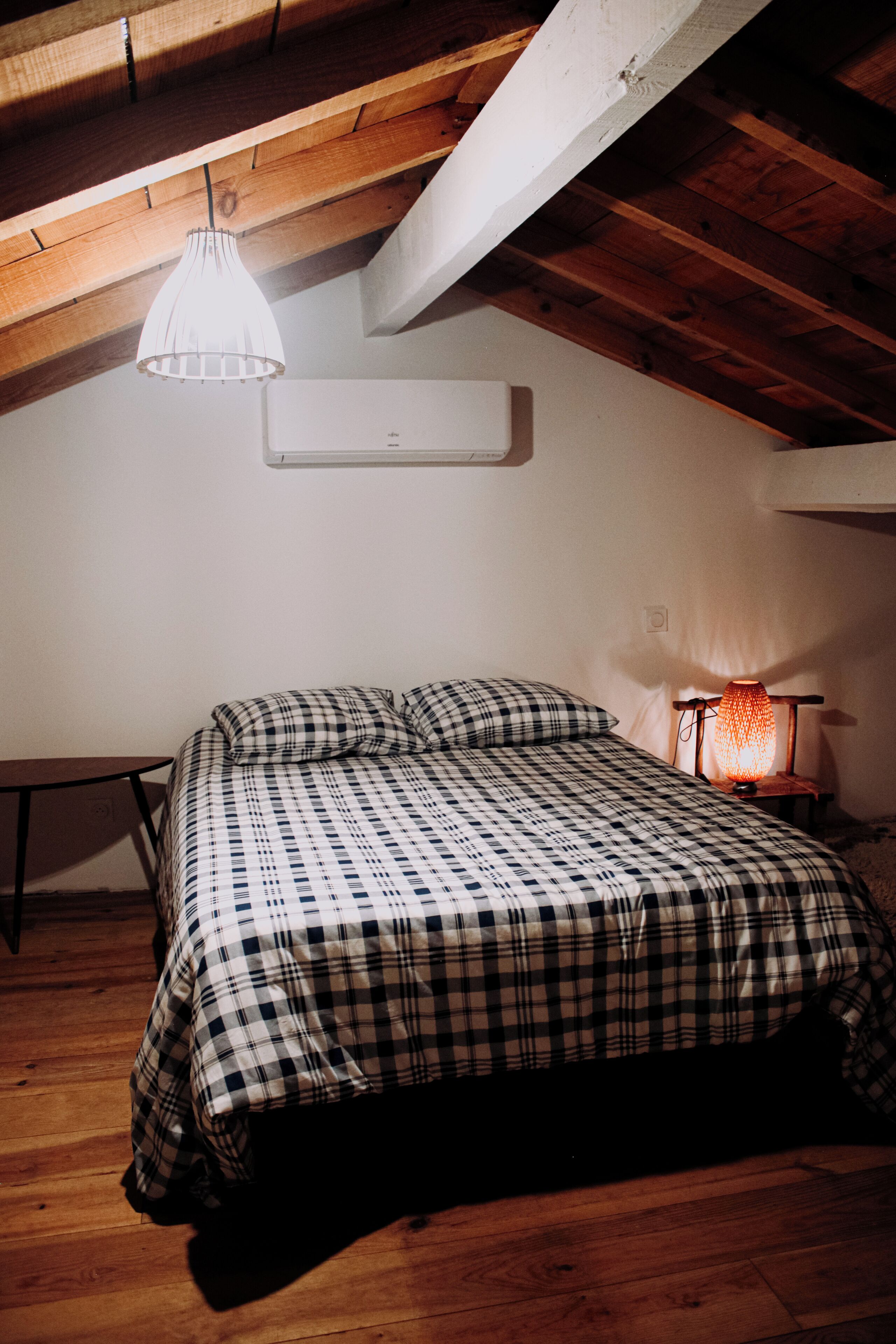 A bedroom with a checkered bedspread, a bedside table, a lamp, and a sloped ceiling.