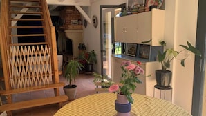 A cozy room with a wooden staircase, a round table with a grid tablecloth, potted plants, and a cabinet with decorative items.