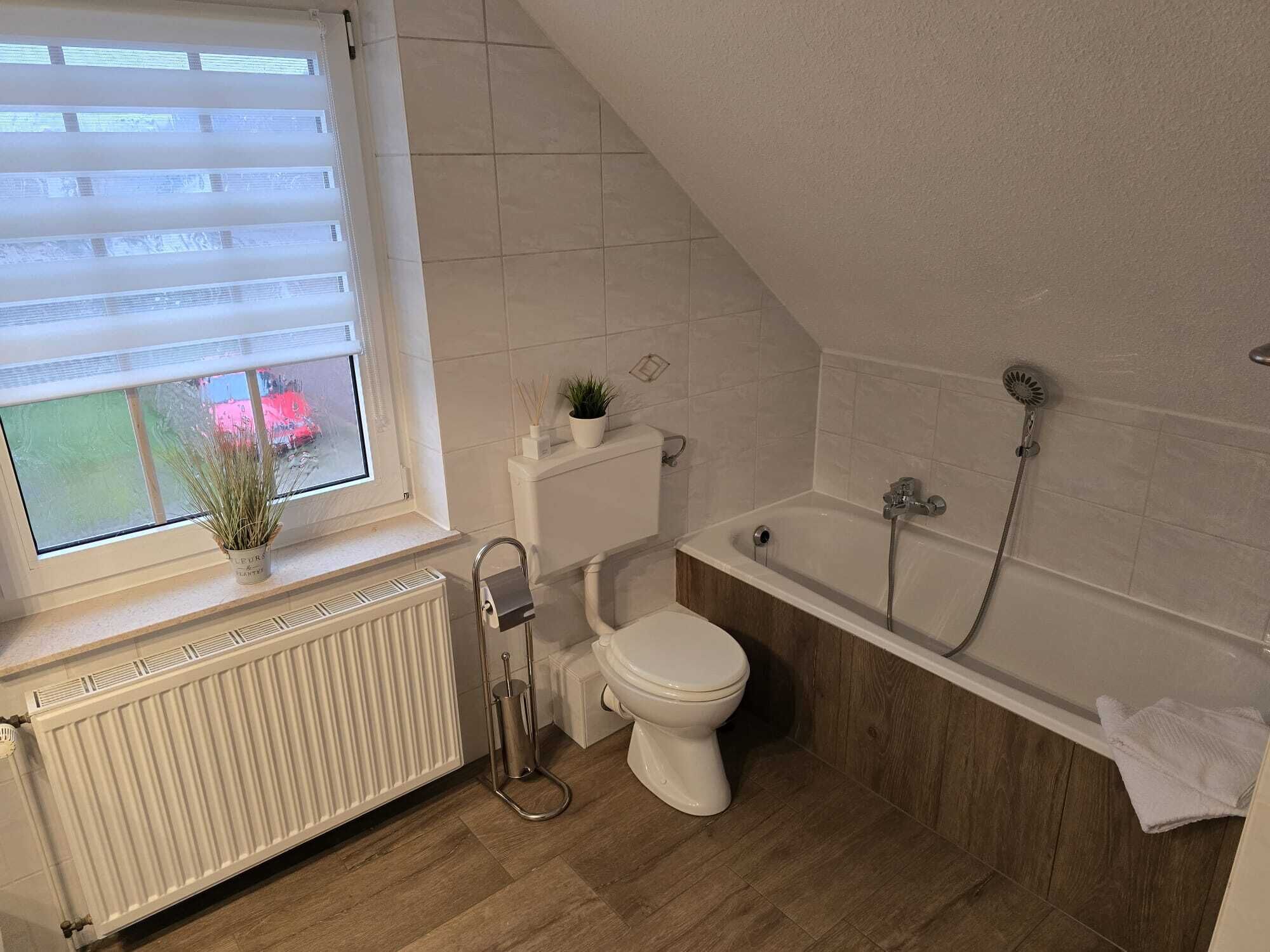 A bathroom with a toilet, a bathtub, a radiator, and a window with blinds.