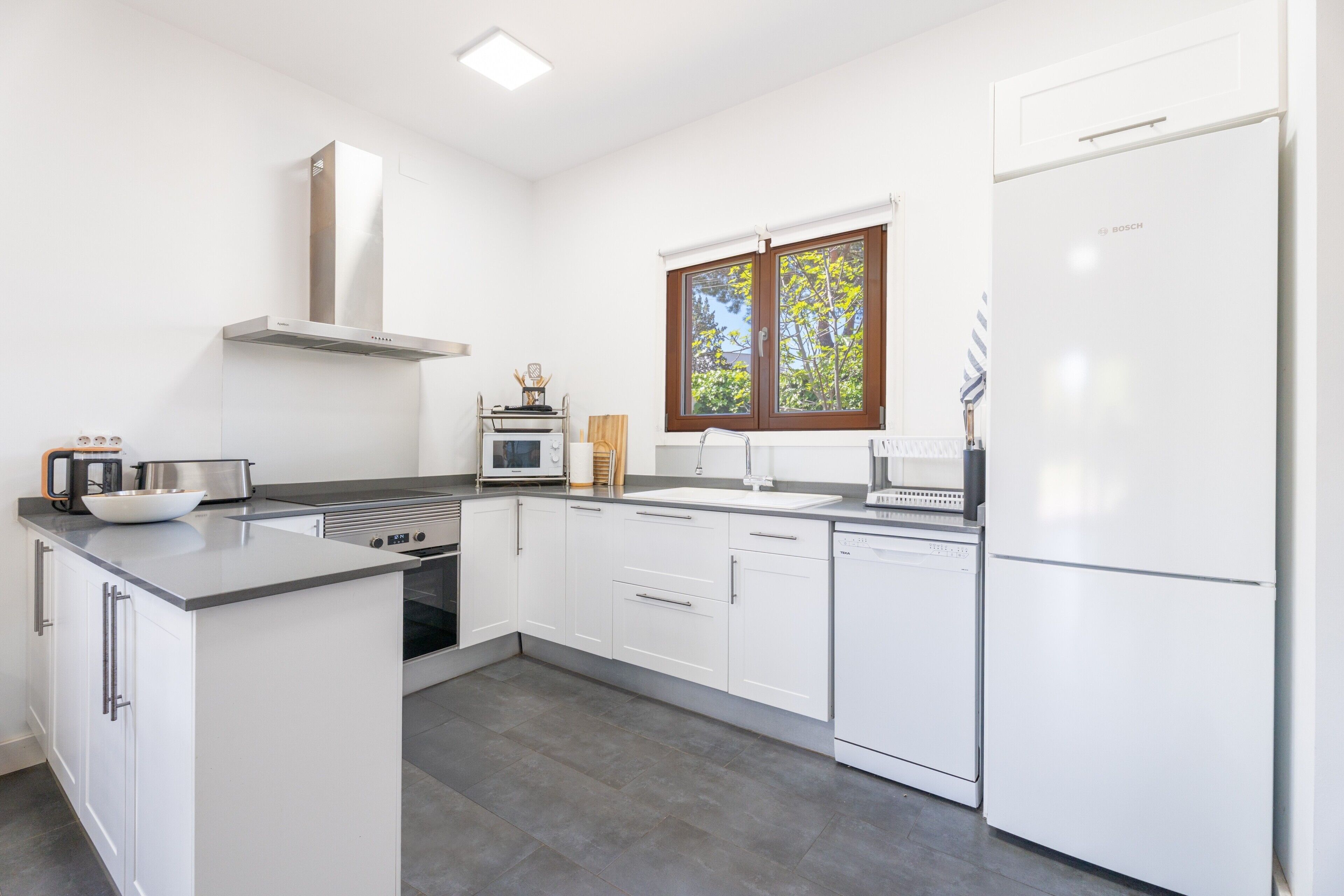 Una cocina moderna con armarios blancos, horno empotrado, microondas y refrigerador Bosch.