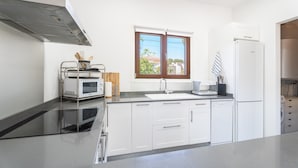Une cuisine moderne avec des meubles blancs, une hotte de cuisinière en acier inoxydable, une fenêtre avec stores et un lave-vaisselle encastré.