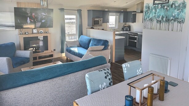 A modern living room with a sofa, a TV, and a dining area with a table. - Sea Front 2 Bedroom Lodge (Honeysuckle 95) at Trecco Bay Holiday Park, Porthcawl (Porthcawl)