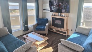 A cozy living room with a large TV, comfortable seating, and a view of the beach. - Sea Front 2 Bedroom Lodge (Honeysuckle 95) at Trecco Bay Holiday Park, Porthcawl (Porthcawl)