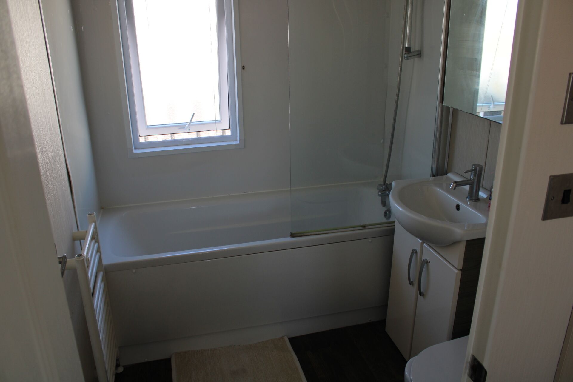 A small, clean bathroom with a bathtub, a sink, and a toilet. There is a window providing natural light.
