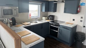 A compact kitchen with a microwave, toaster, sink, stove, and wooden cutting boards. - Sea Front 2 Bedroom Lodge (Honeysuckle 95) at Trecco Bay Holiday Park, Porthcawl (Porthcawl)