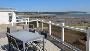 A deck with outdoor furniture overlooking a beach. - Sea Front 2 Bedroom Lodge (Honeysuckle 95) at Trecco Bay Holiday Park, Porthcawl (Porthcawl)