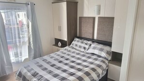A bedroom with a bed, a wardrobe, and a window with curtains. - Sea Front 2 Bedroom Lodge (Honeysuckle 95) at Trecco Bay Holiday Park, Porthcawl (Porthcawl)