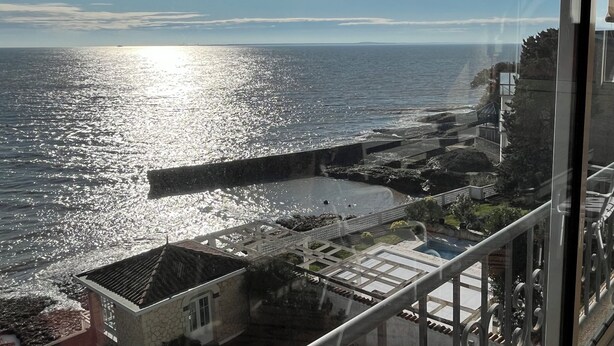 A coastal view from a balcony with a clear sky, a rocky shoreline, and a building with a stone facade. - QUIET PIED A MER WITH EXCEPTIONAL VIEWS AND CLOSE TO RESORT CENTER (Saint-Palais-sur-Mer)