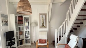 A living room with a bookshelf, a television, a wicker lamp, a chair, and a staircase. - QUIET PIED A MER WITH EXCEPTIONAL VIEWS AND CLOSE TO RESORT CENTER (Saint-Palais-sur-Mer)