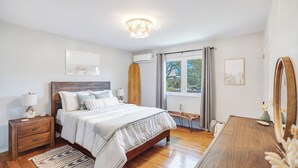 Une chambre à coucher avec un lit en bois, des tables de chevet, une commode, un miroir et une fenêtre avec des rideaux.