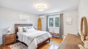 Une chambre à coucher avec un lit en bois, des tables de chevet, une commode, un miroir et une fenêtre avec des rideaux.