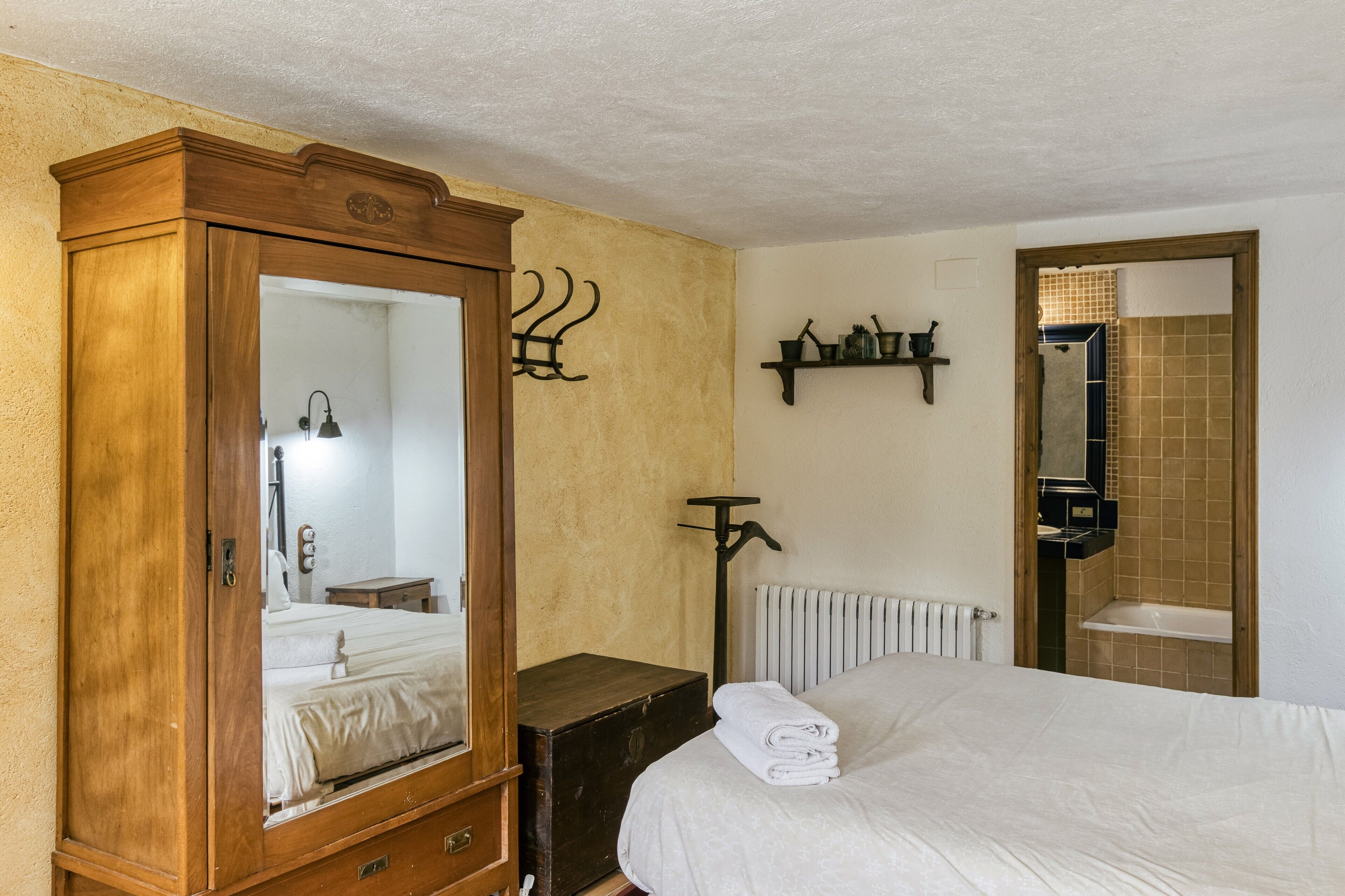 Un dormitorio con un armario de madera, una cama con edredón blanco, un radiador y una estantería con artículos de aseo.