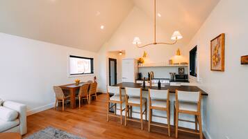 A modern kitchen with wooden flooring, a dining area with chairs, and a central island.