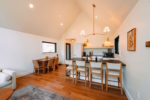 A modern kitchen with wooden flooring, a dining area with chairs, and a central island.