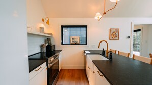 A compact kitchen with a black countertop, white cabinets, a window, and a sink. - Maynard's Retreat | Hocking Hills, Modern, Hot Tub (Rockbridge)