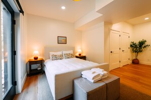 A hotel room with a large bed, two bedside tables with lamps, a potted plant, and a view of the outside. - Maynard's Retreat | Hocking Hills, Modern, Hot Tub (Rockbridge)