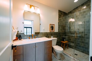 Un baño con lavamanos blanco, armarios de madera, inodoro y cabina de ducha con mampara de vidrio.