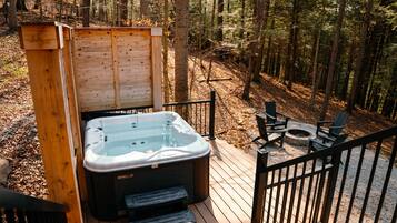 A hot tub on a wooden deck with a wooden structure behind it, surrounded by a forest.