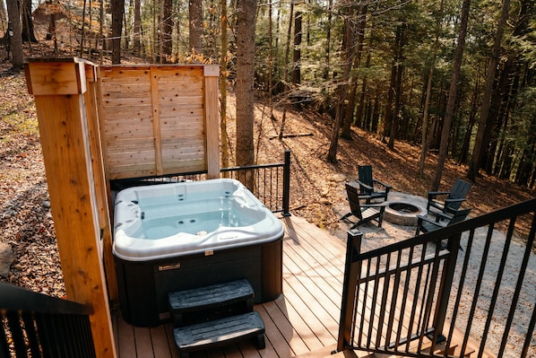 A hot tub on a wooden deck with a wooden structure behind it, surrounded by a forest.