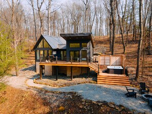 A modern cabin with a deck, a hot tub, and a fire pit.