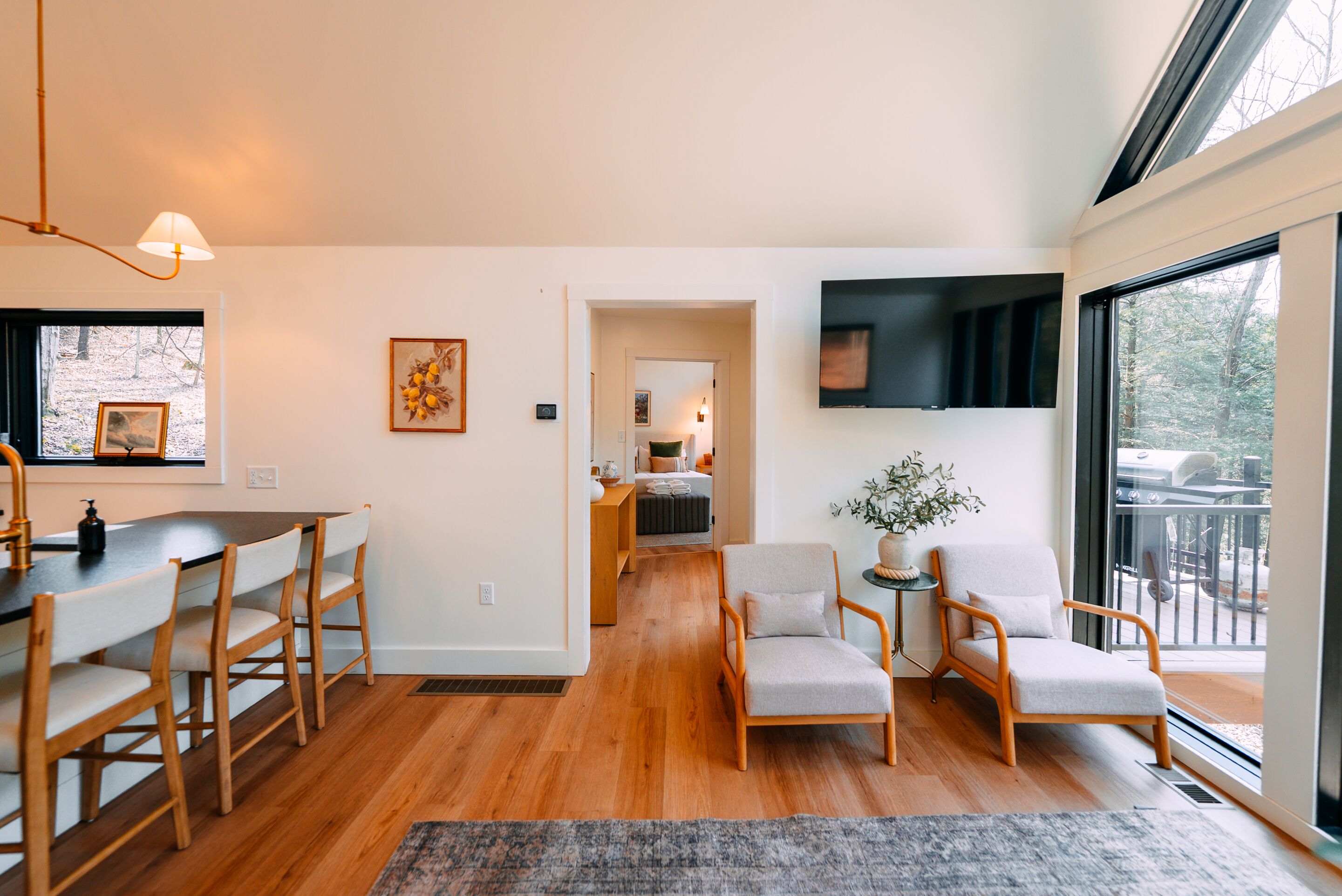 A modern living room with a dining area, a large window, and a TV mounted on the wall.