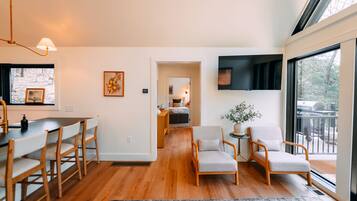A modern living room with a dining area, a large window, and a TV mounted on the wall.