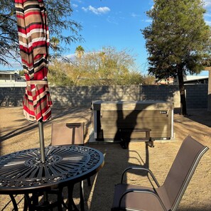 An outdoor patio with a metal table and chairs, a striped umbrella, and a portable heater. - Hot tub stargazing, pet friendly! Downtown & hiking nearby. (Tucson)