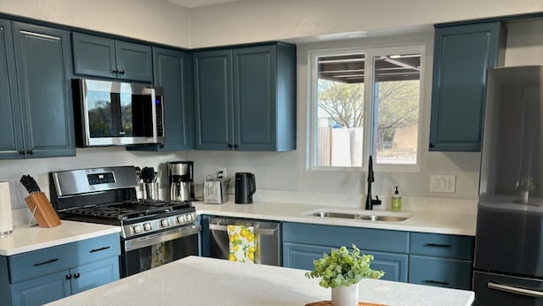 A modern kitchen with blue cabinets, stainless steel appliances, a central island, and a view of the outdoors. - Hot tub stargazing, pet friendly! Downtown & hiking nearby. (Tucson)