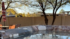 Una vasca idromassaggio con coperchio in vetro trasparente, circondata da alberi e da un’area patio con sedie.