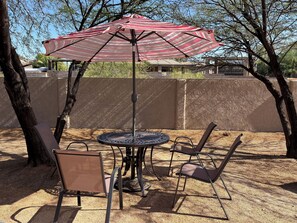 A round metal table with a striped umbrella, two chairs, and a tree in a backyard setting. - Hot tub stargazing, pet friendly! Downtown & hiking nearby. (Tucson)