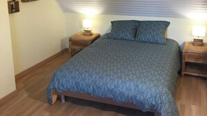 A bedroom with a sloped ceiling, a bed with a patterned bedspread, two bedside tables with lamps, and a hanging light fixture. - Breton cottage in the countryside, calm & comfort (Locoal-Mendon)