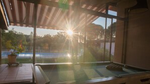 A pool table under a roof with a view of a body of water and trees.