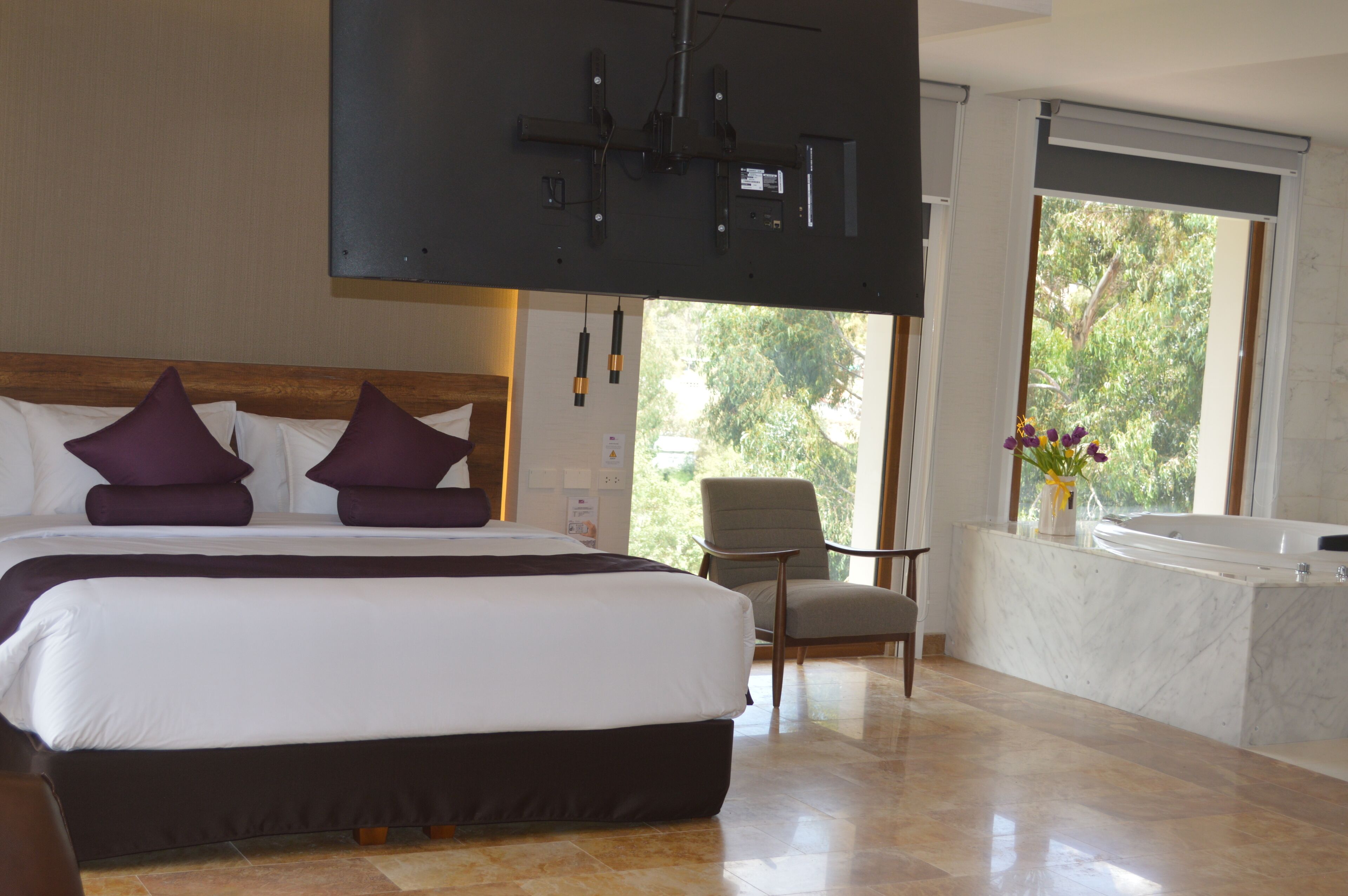 Une chambre d’hôtel avec un grand lit, une chaise, une baignoire et un téléviseur fixé au mur.