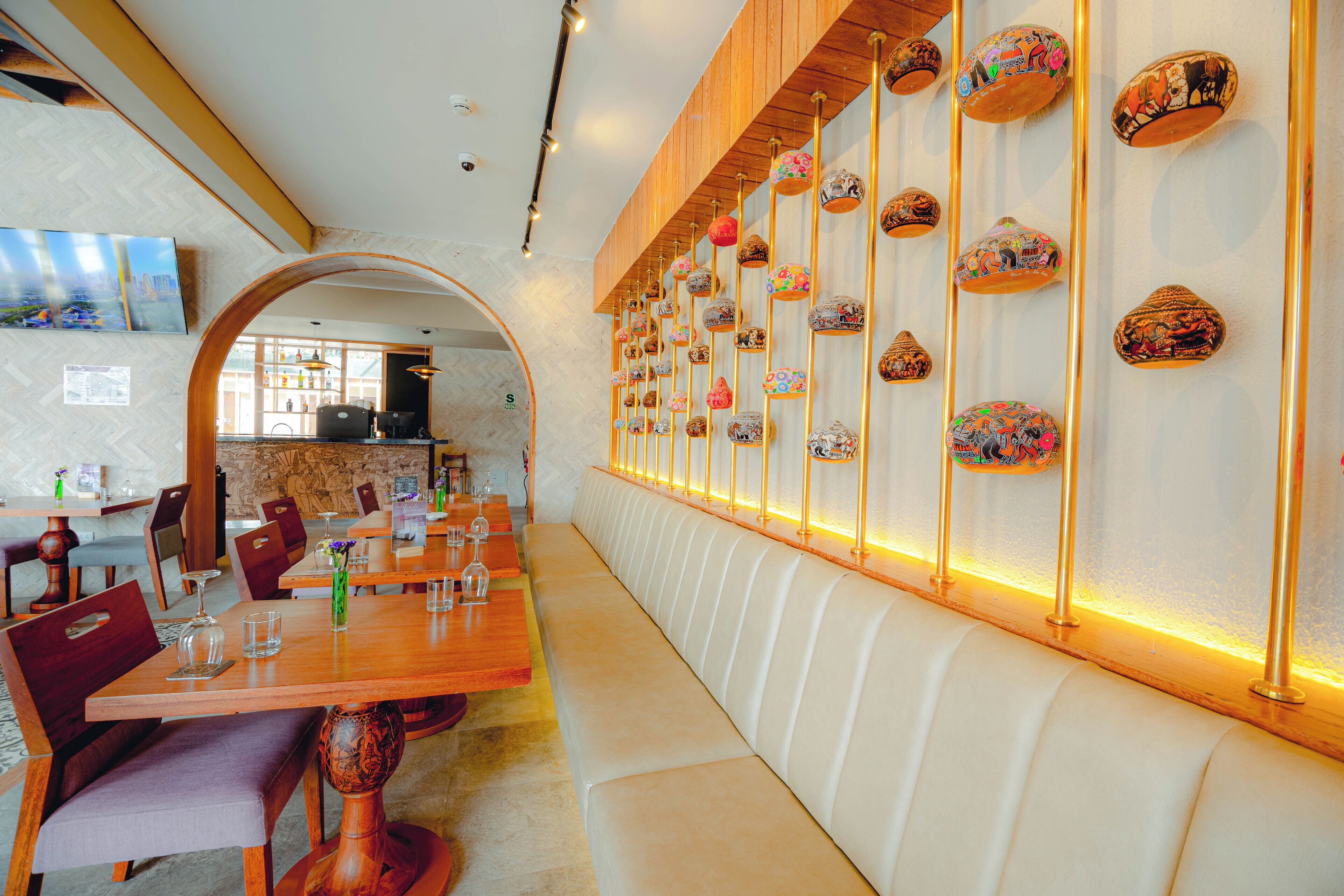 Un restaurante con un largo banco de madera, mesas con sillas y una pared decorada con cerámica.