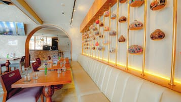 A restaurant with a long wooden bench, tables with chairs, and a wall decorated with pottery.