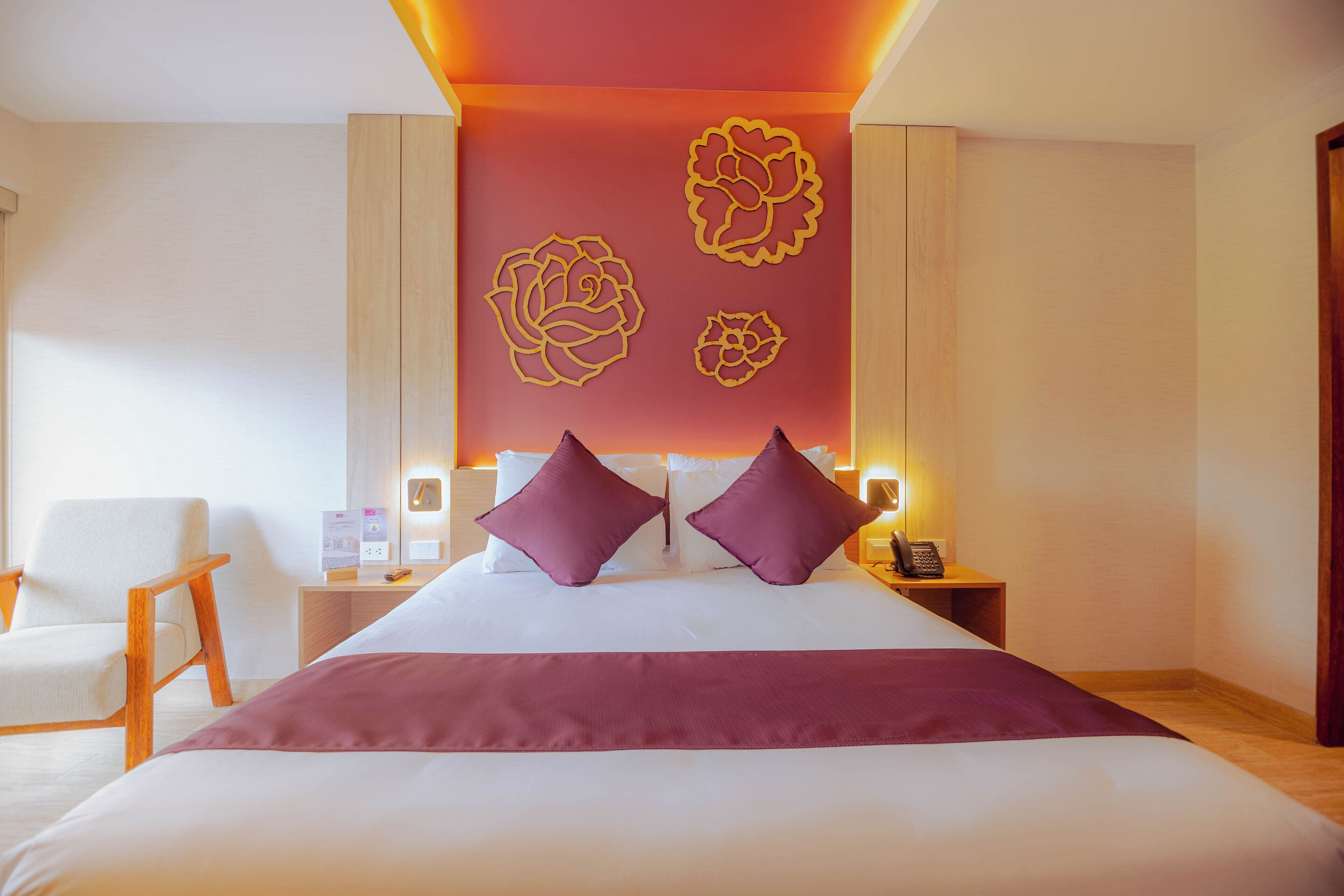 Ein Hotelzimmer mit einem großen Bett, zwei Kissen, einem Nachttisch mit Telefon und einer Wand mit floralen Verzierungen.