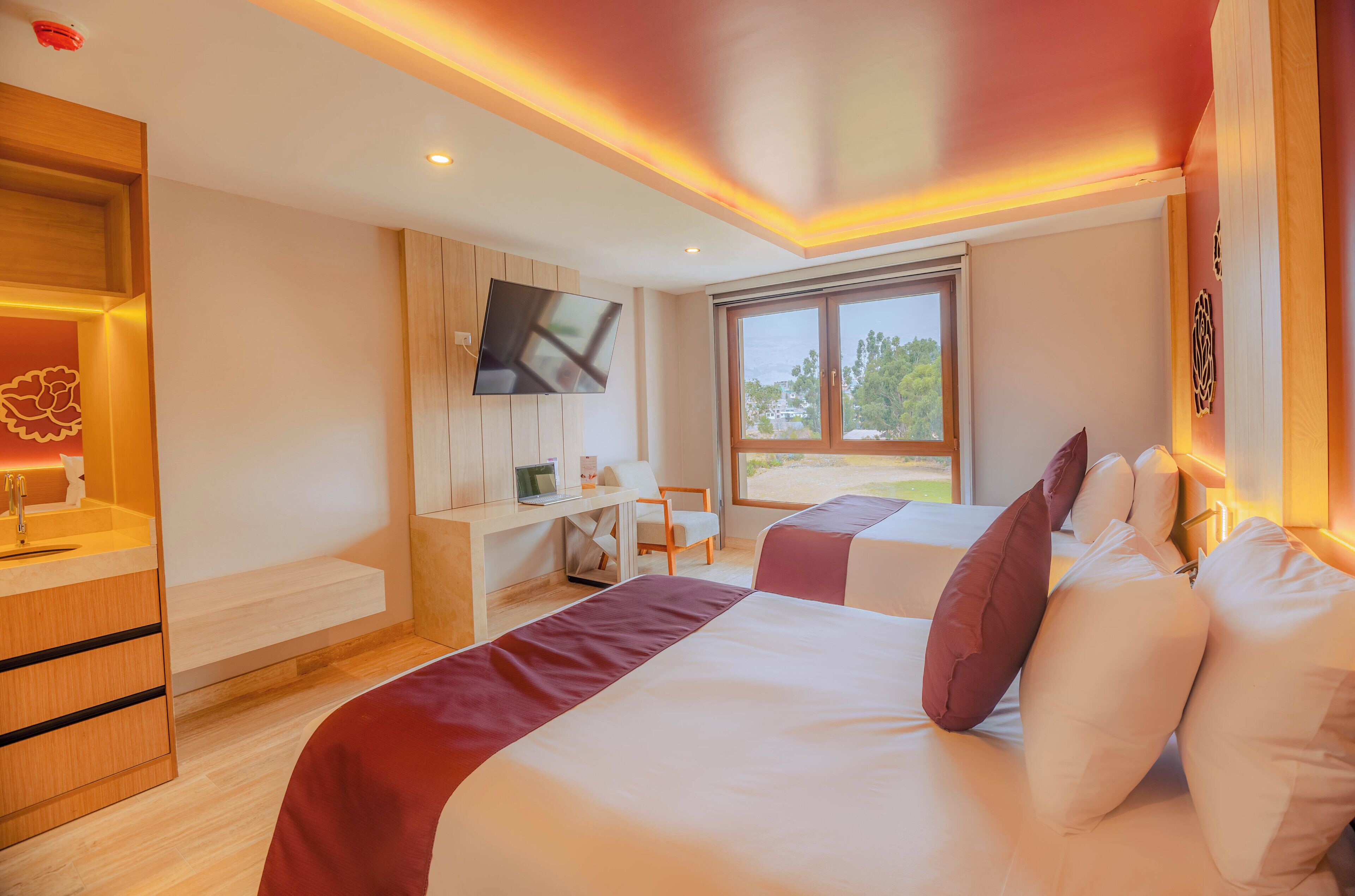 A hotel room with a bed, desk, TV, and a window with a view of greenery.