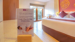 Een hotelkamer met een groot bed, een houten hoofdbord, een nachtkastje, een lamp en een poster met een aanbieding voor later uitchecken.