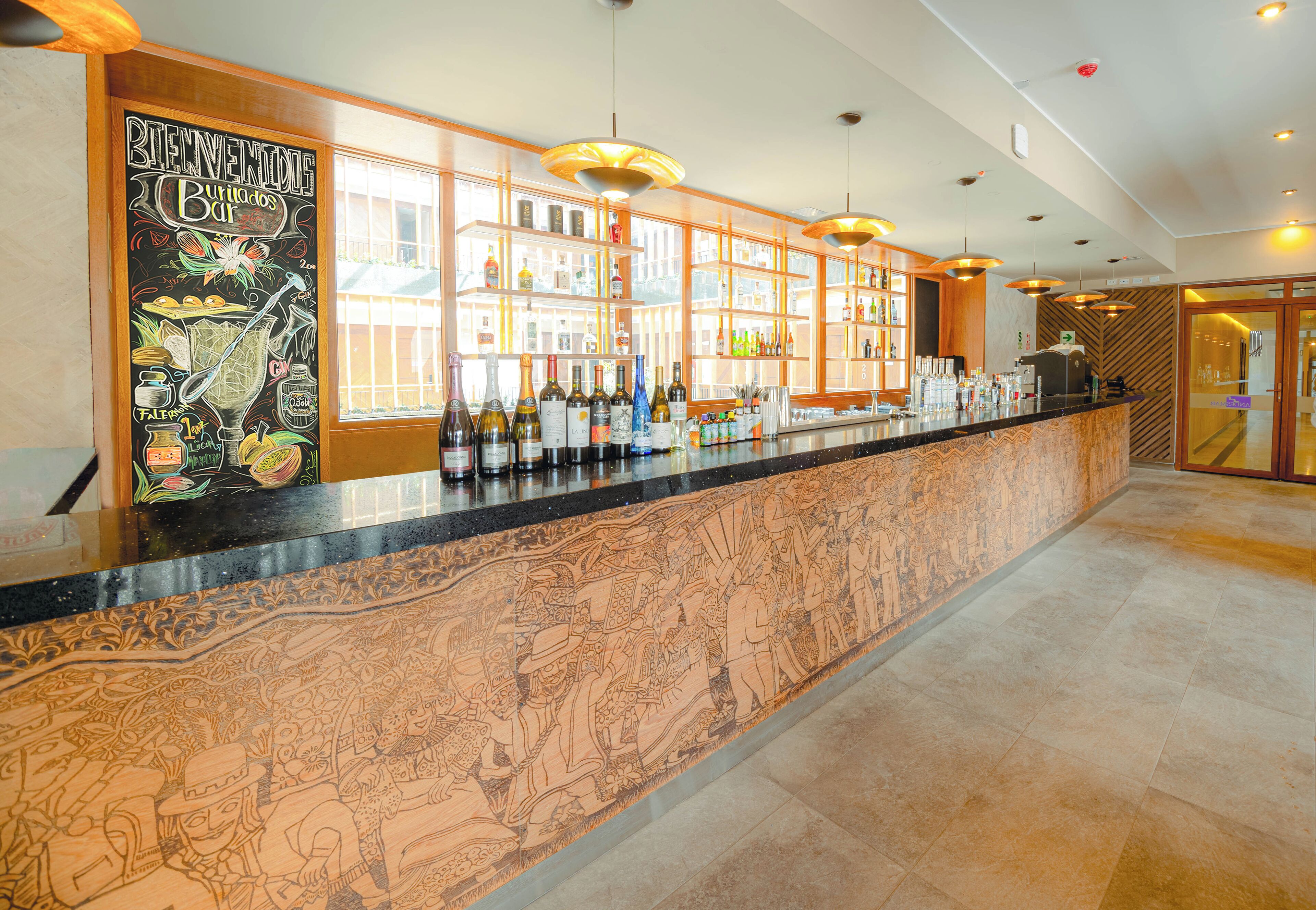A bar area with a long counter, shelves with bottles, and a mural on the wall.
