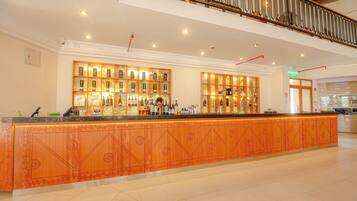 A hotel reception area with a long counter, two wooden display shelves filled with bottles, and a sign indicating the exit.