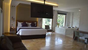 A spacious bedroom with a large bed, a sitting area with a sofa, a TV mounted on the wall, and a bathroom with a bathtub and sink.
